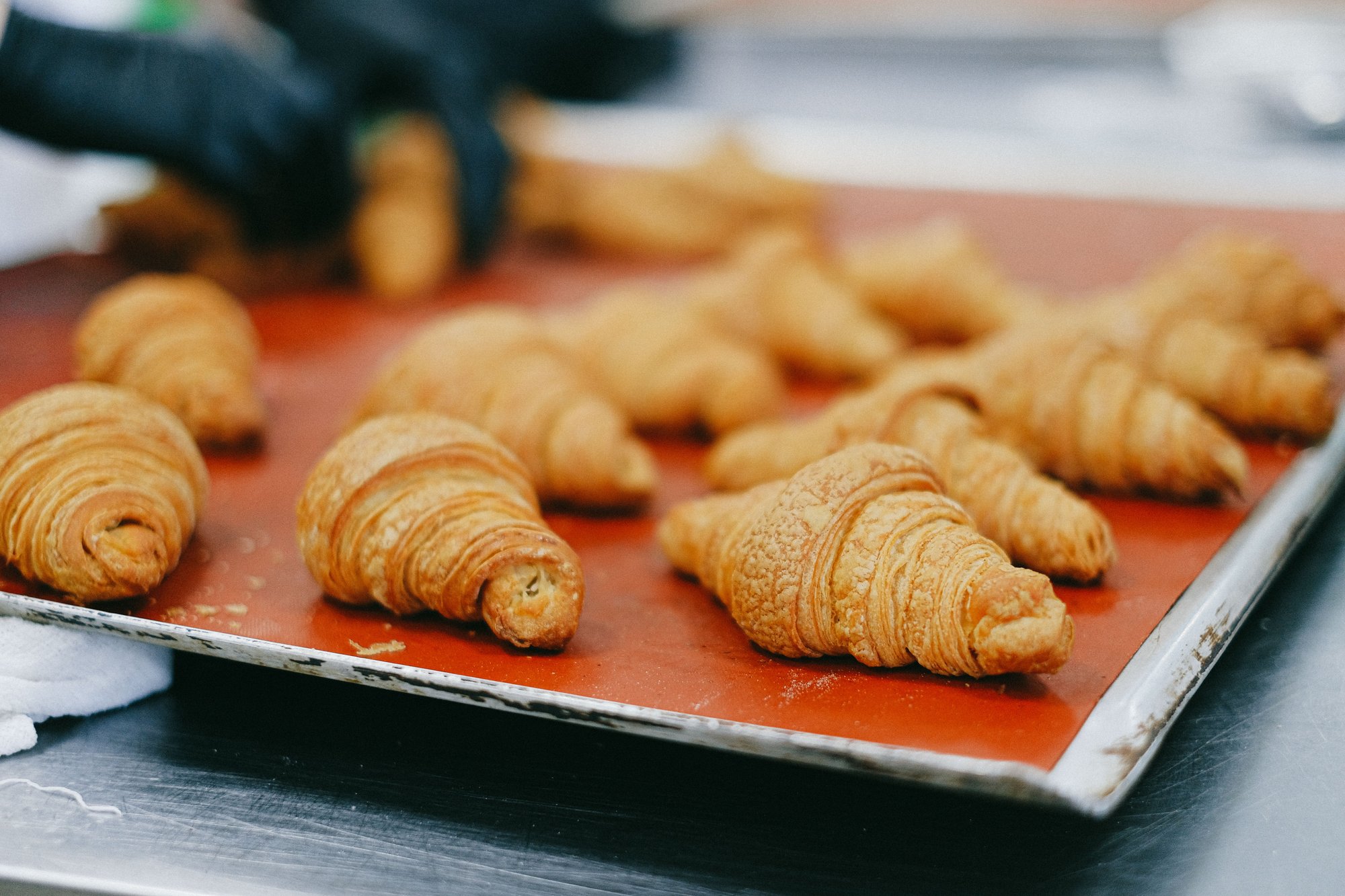 Golden croissants lined up on a red baking mat, just out of the oven.
