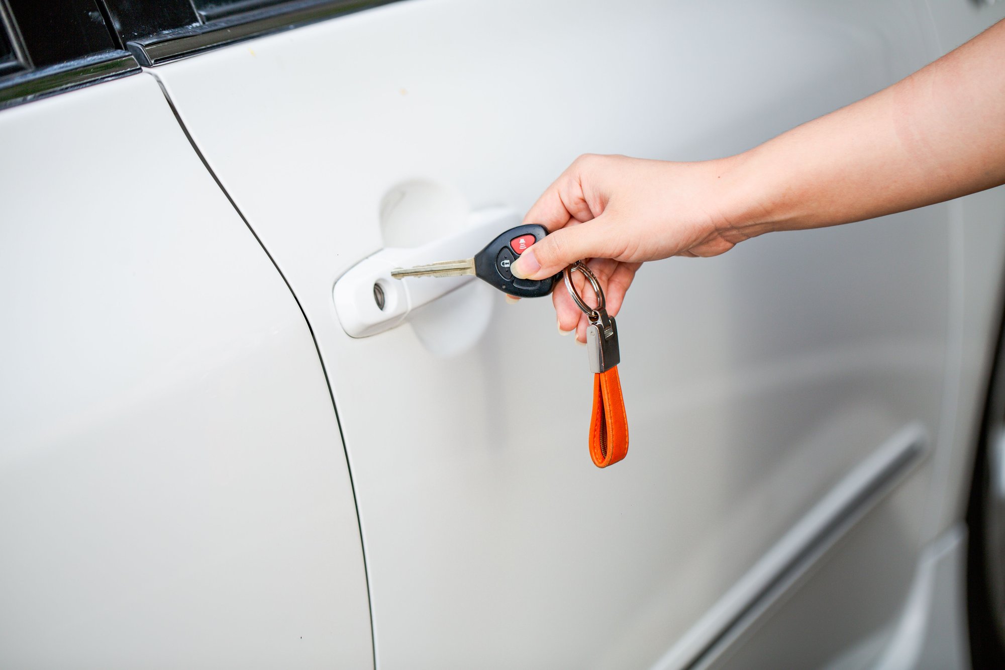 A hand fitting a key into the driver&rsquo;s door of a white car.