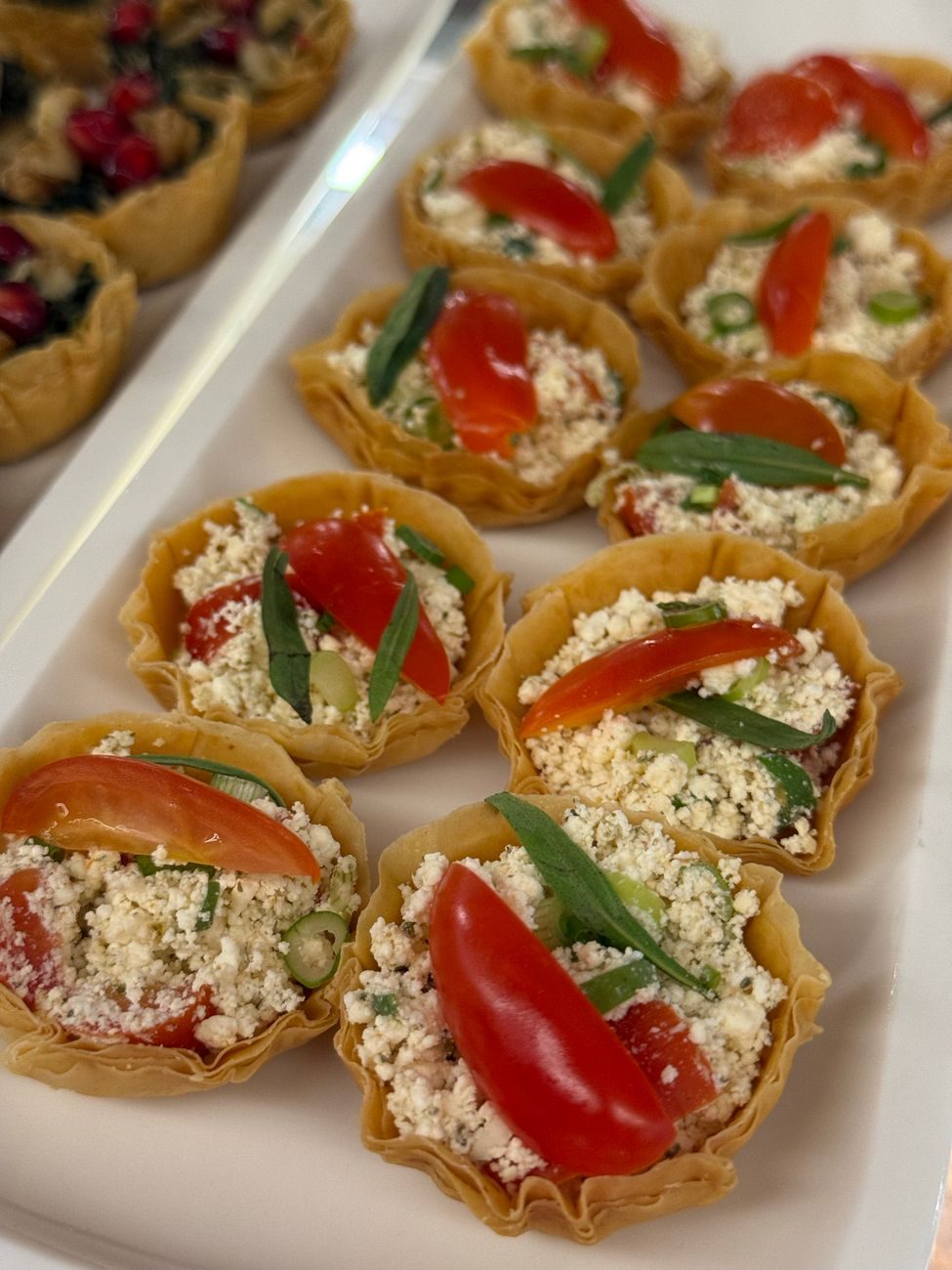 Phyllo tartlets filled with herbed cheese, tomato and tarragon, lined up in rows on a white platter