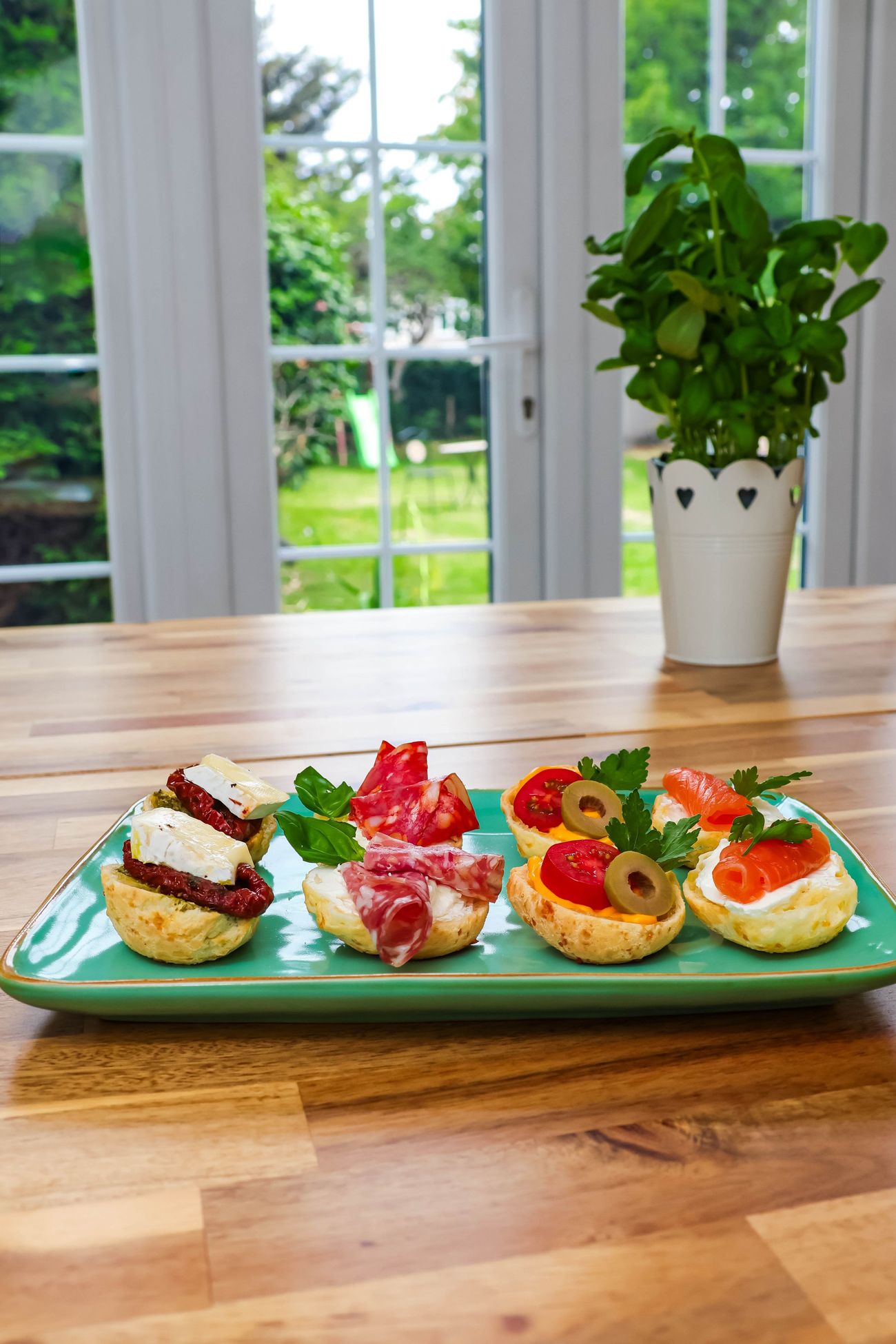 A plate of canap&eacute;s on a wooden bench beside a window looking onto the garden
