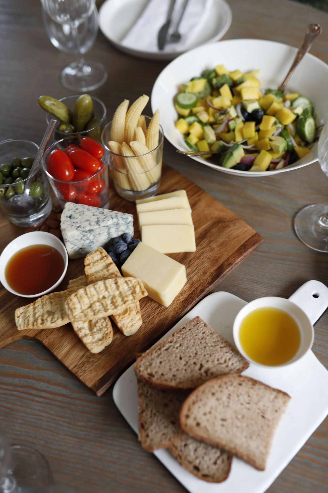 Seen from above: a cheese board, a bowl of salad, olives and sliced bread set out together
