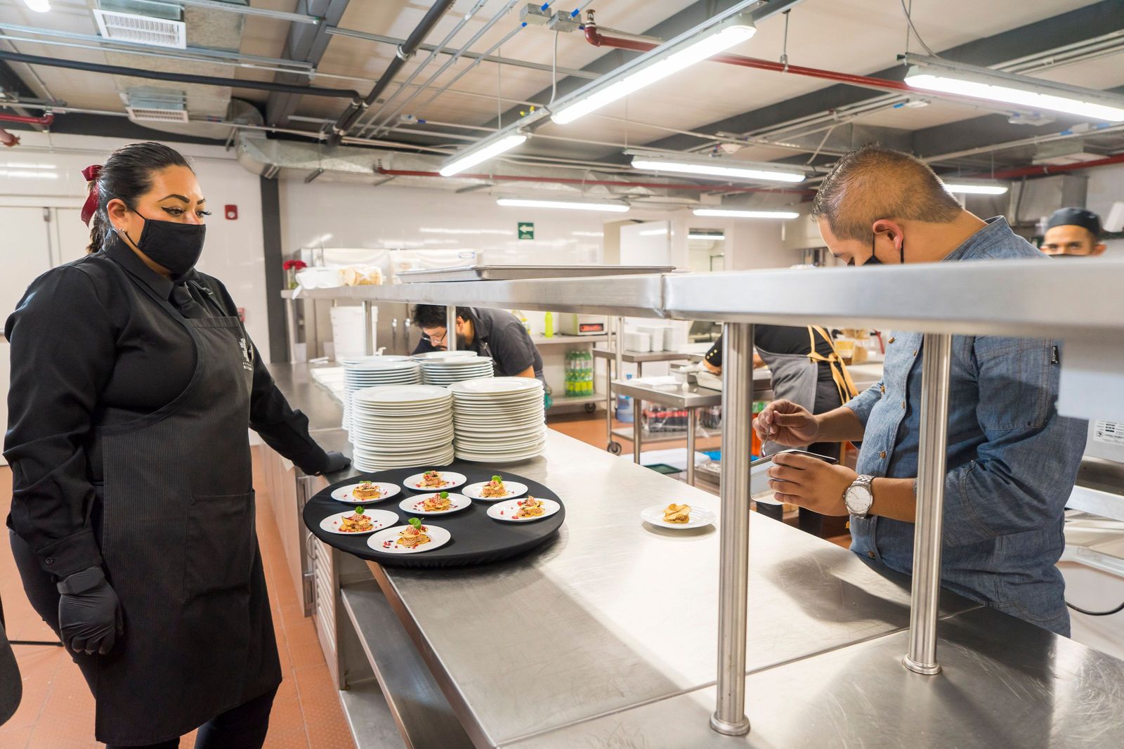 A kitchen mid-service, plates lined up down the pass and cooks working along them