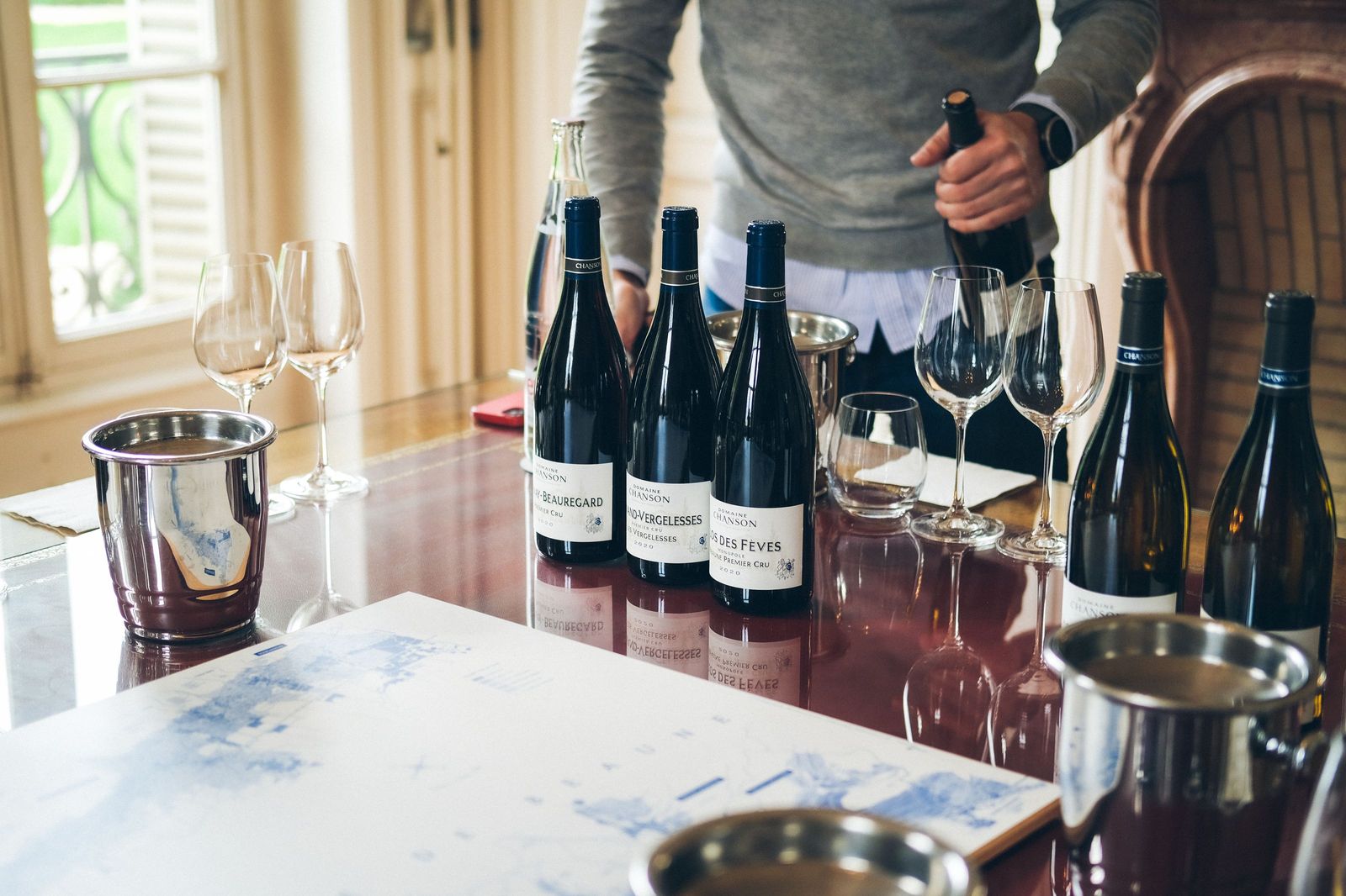 Wine being poured into glasses at a laid table, bottles standing alongside