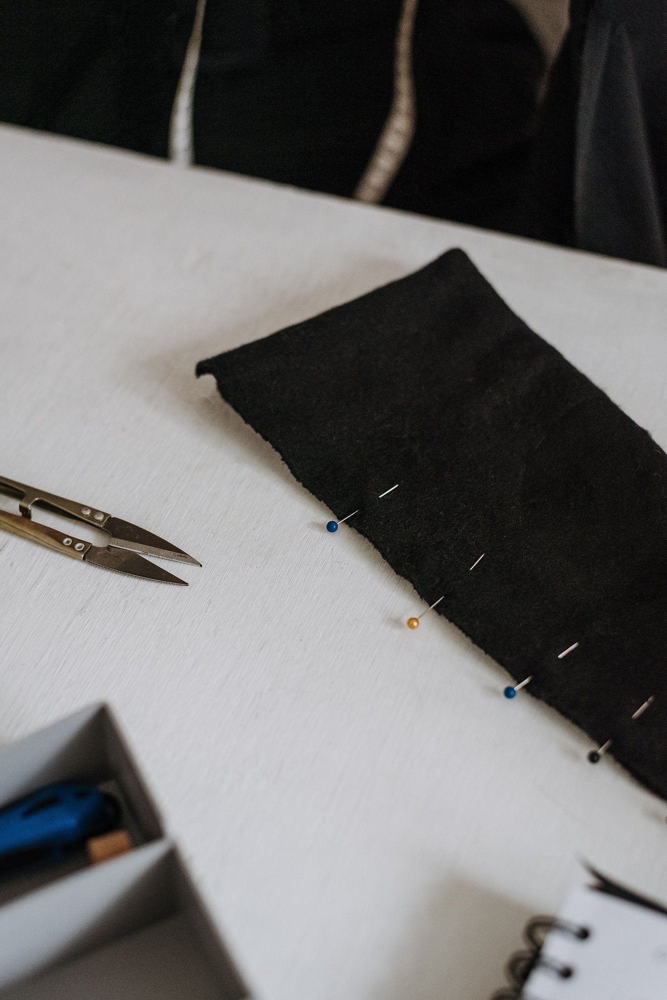 Pins holding a folded hem in place on dark fabric, ready for sewing.