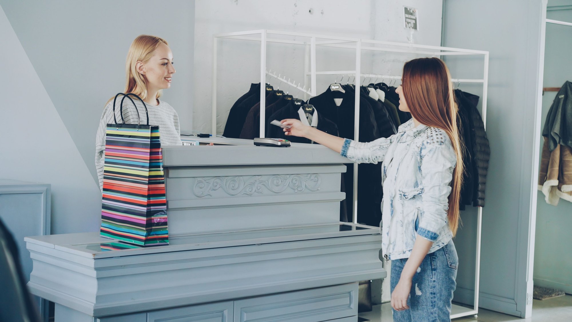 A customer at a white counter with racks of finished garments behind it.