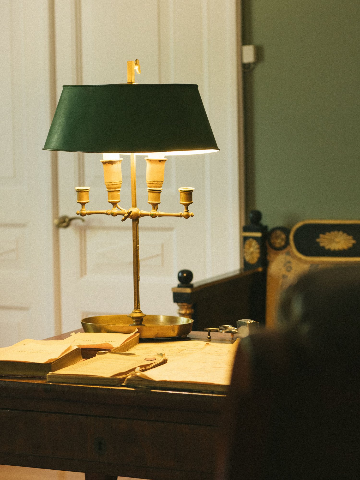 A brass lamp with a green shade throwing warm light over papers on a desk.