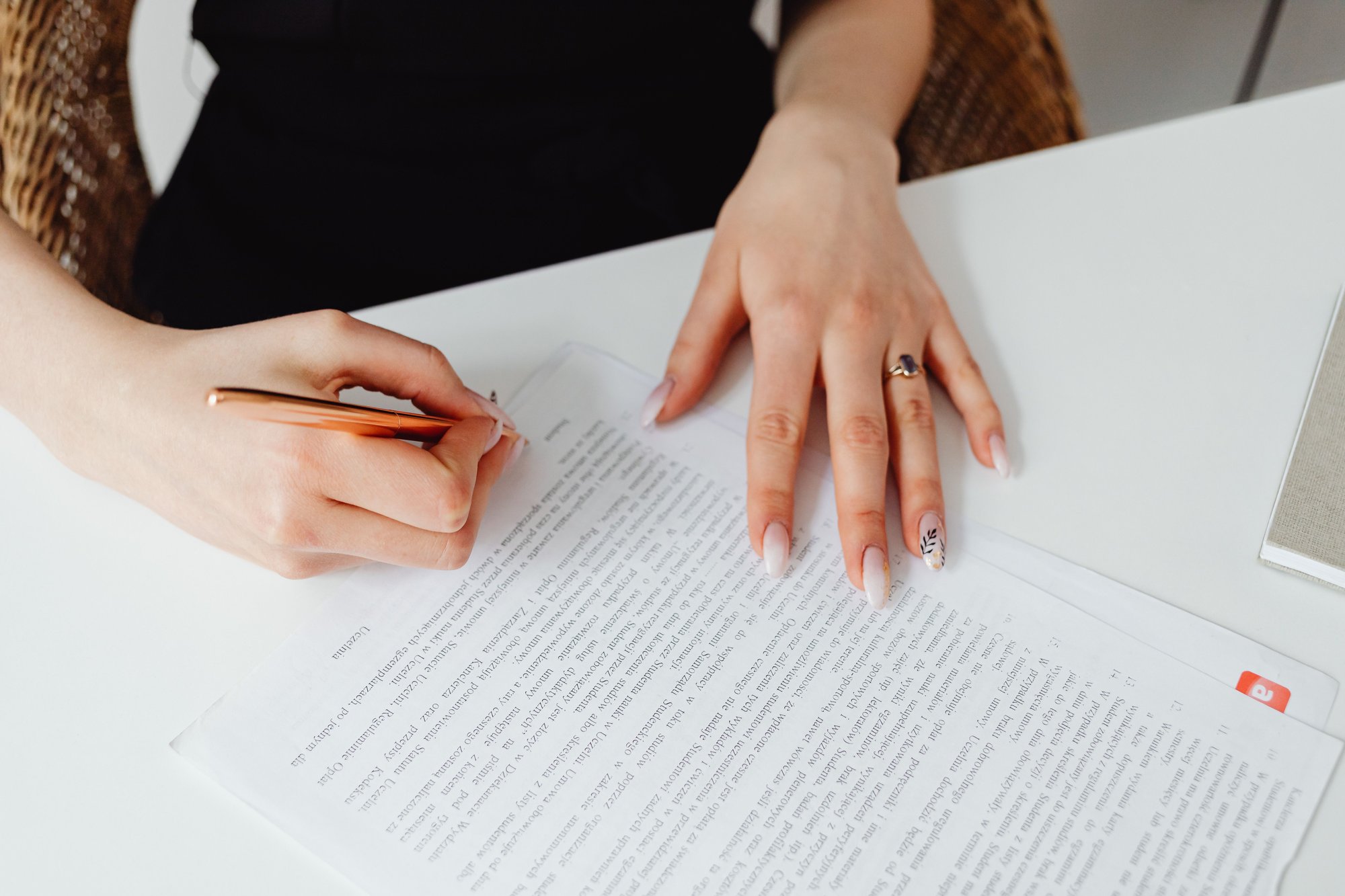 A woman’s hand with a pen over a printed contract beside a laptop.