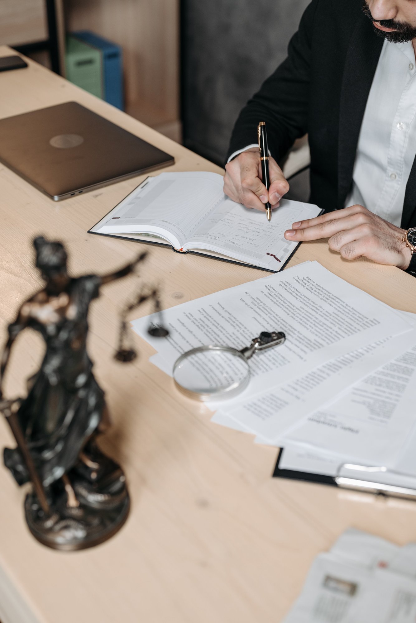 A figure of Justice, a magnifying glass and a printed document on a pale desk.