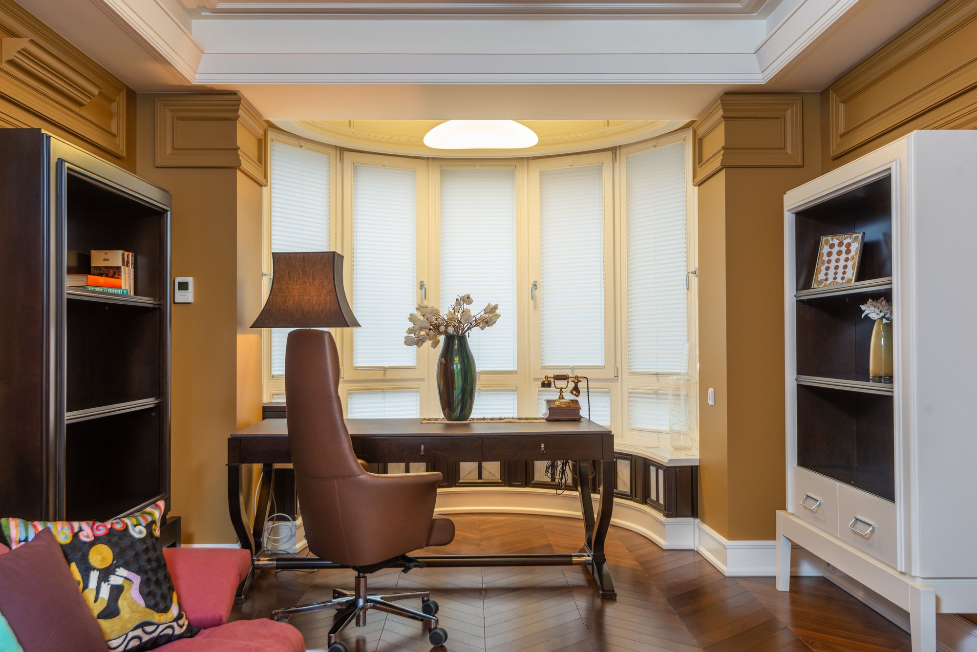 A calm office: a leather armchair, a wooden desk, a lamp and a vase of dried flowers.