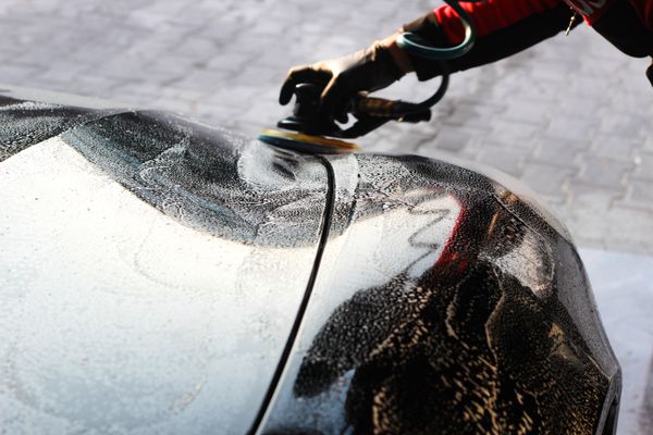 A detailer running a machine polisher across a foam-covered car panel