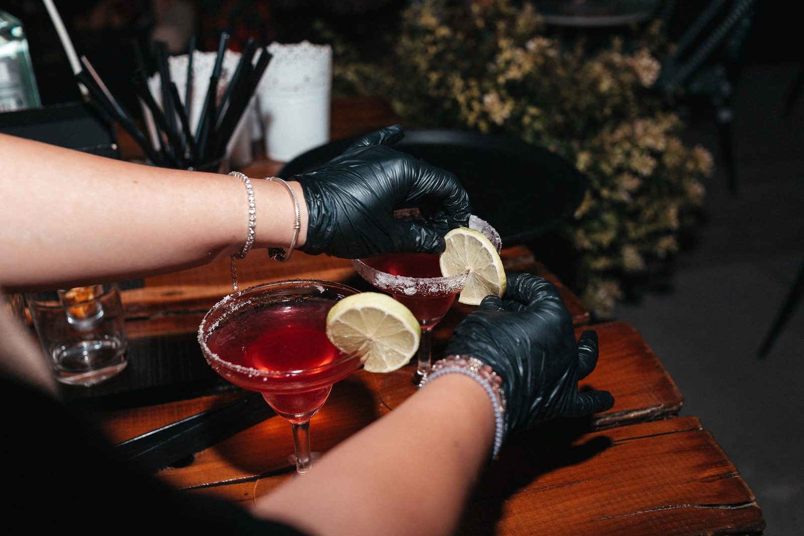 A bartender&rsquo;s hands finishing two cocktails with slices of lemon on a dark wooden bar.